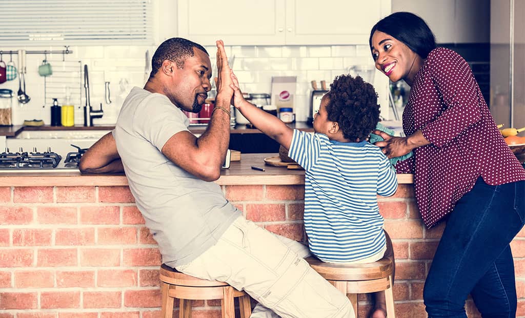 Young dad smiling and high-fiving young son while mom watches and smiles